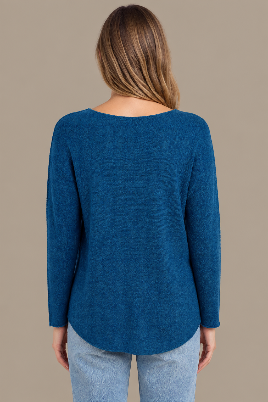 Denimblaues Langarm-Strickoberteil am Modell von hinten vor Greige-Hintergrund