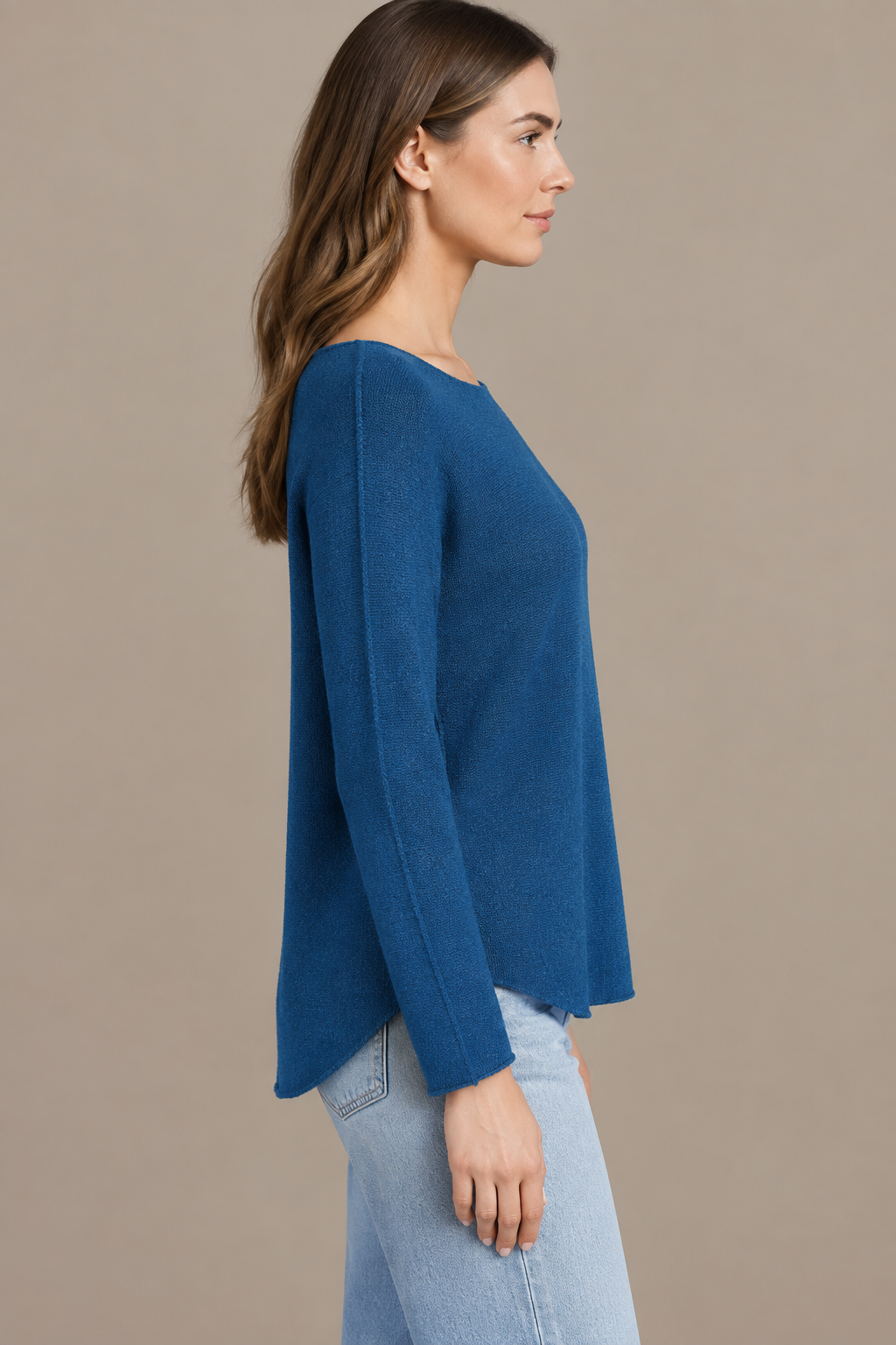 Denimblaues Langarm-Strickoberteil am Modell von der Seite vor Greige-Hintergrund