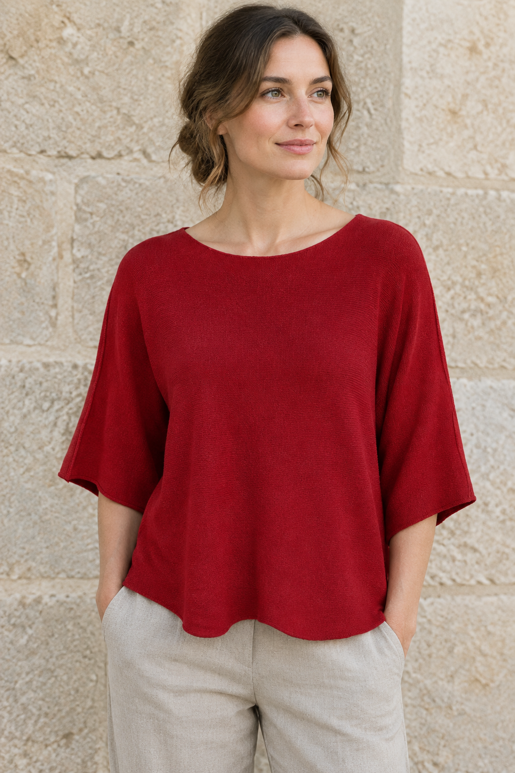 Rotes Strickoberteil am Modell vor Steinwand